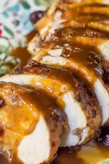 Tender sliced turkey breast on vintage floral plate with caramelized cranberry glaze drizzled between each slice, whole cranberries scattered around, golden sauce visible