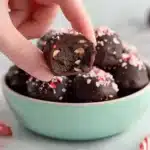 Hand holding a half-eaten chocolate peppermint truffle with crunchy nuts and crushed candy cane topping, healthy holiday dessert digital recipe PDF.