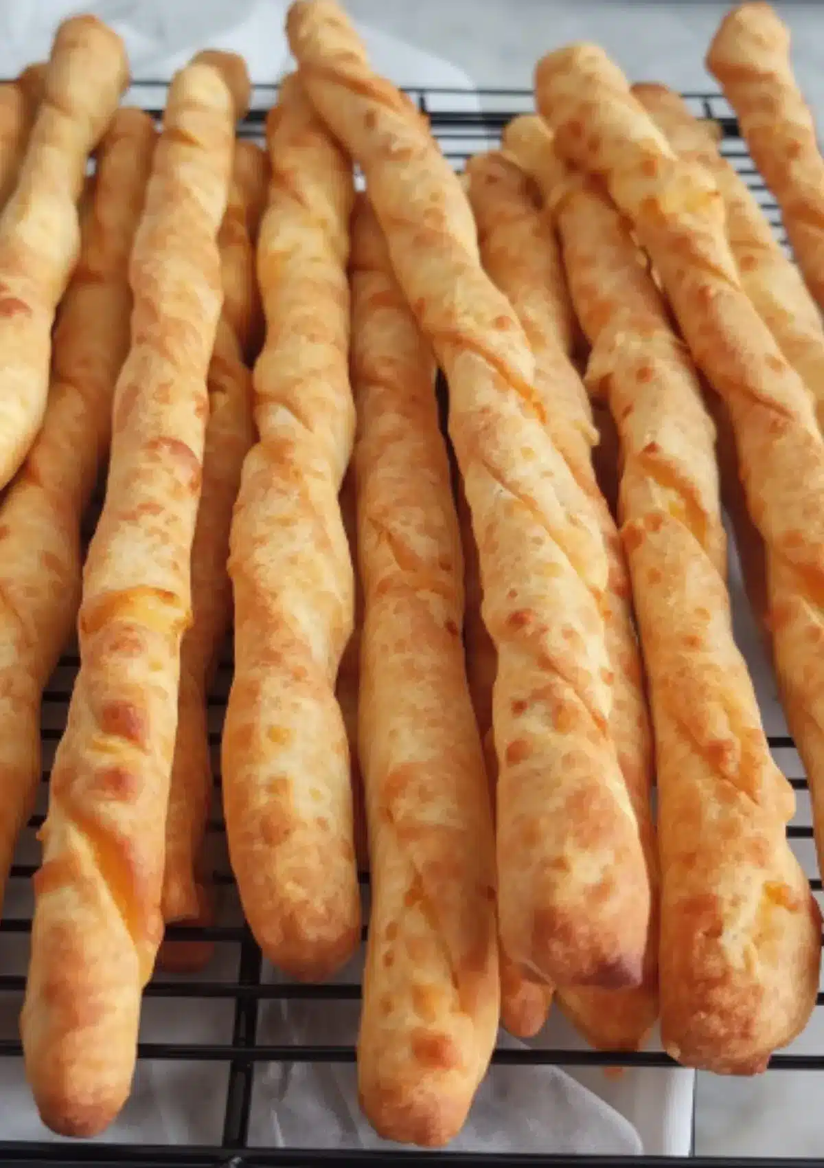 Close-up overhead view of freshly baked golden cheddar cheese straws with visible cheese flecks cooling on a wire rack