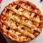 Golden brown apple cranberry pie with lattice crust fresh from the oven surrounded by fresh cranberries and apples
