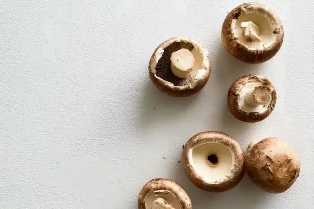 Fresh brown mushrooms with stems removed ready to be filled, arranged on white surface showing preparation stage