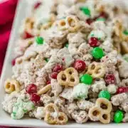 Reindeer chow with thick white chocolate coating on Cheerios, pretzels, peanuts and M&Ms served on white platter with pink textured napkin