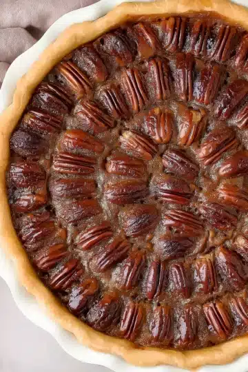 Complete chocolate bourbon pecan pie with glossy filling and symmetrically arranged pecans in white fluted pie dish on pink cloth