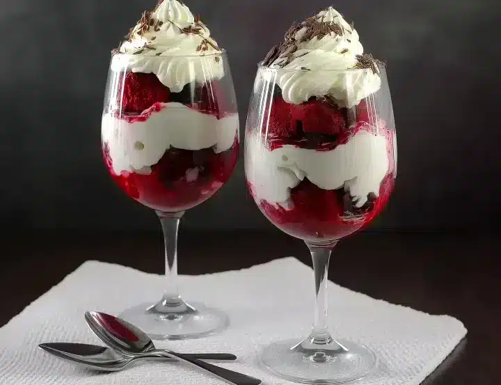 Boozy red velvet trifle desserts layered with cream and topped with chocolate shavings in wine glasses