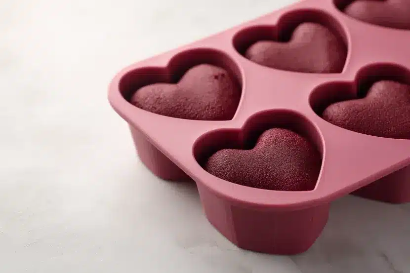 Pink silicone mold with heart-shaped cavities filled with red velvet cake batter for making Valentine's Day cake pops