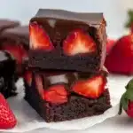 Two stacked chocolate brownies with fresh strawberry pieces embedded inside and glossy chocolate coating on top, surrounded by fresh strawberries
