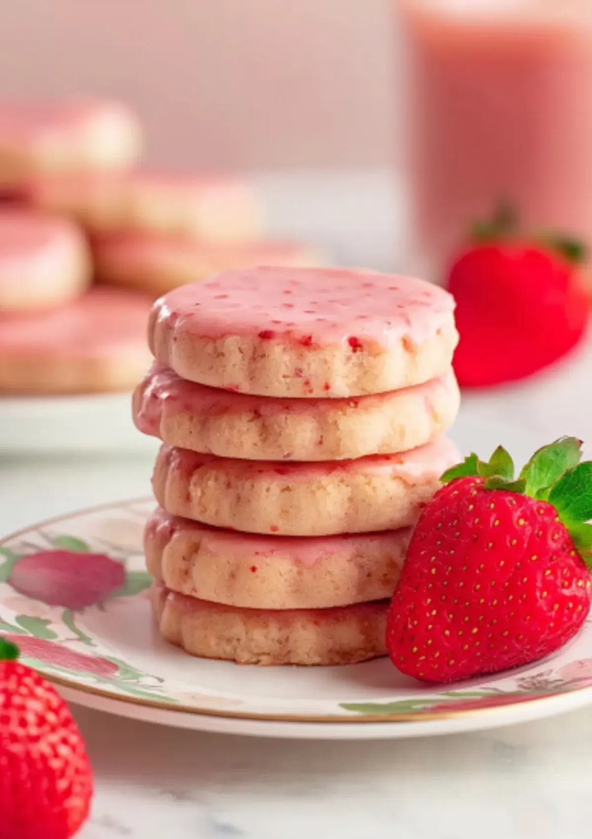 A plate of stacked strawberry shortbread cookies, glazed in pink and surrounded by fresh strawberries, perfect for Valentine’s Day.